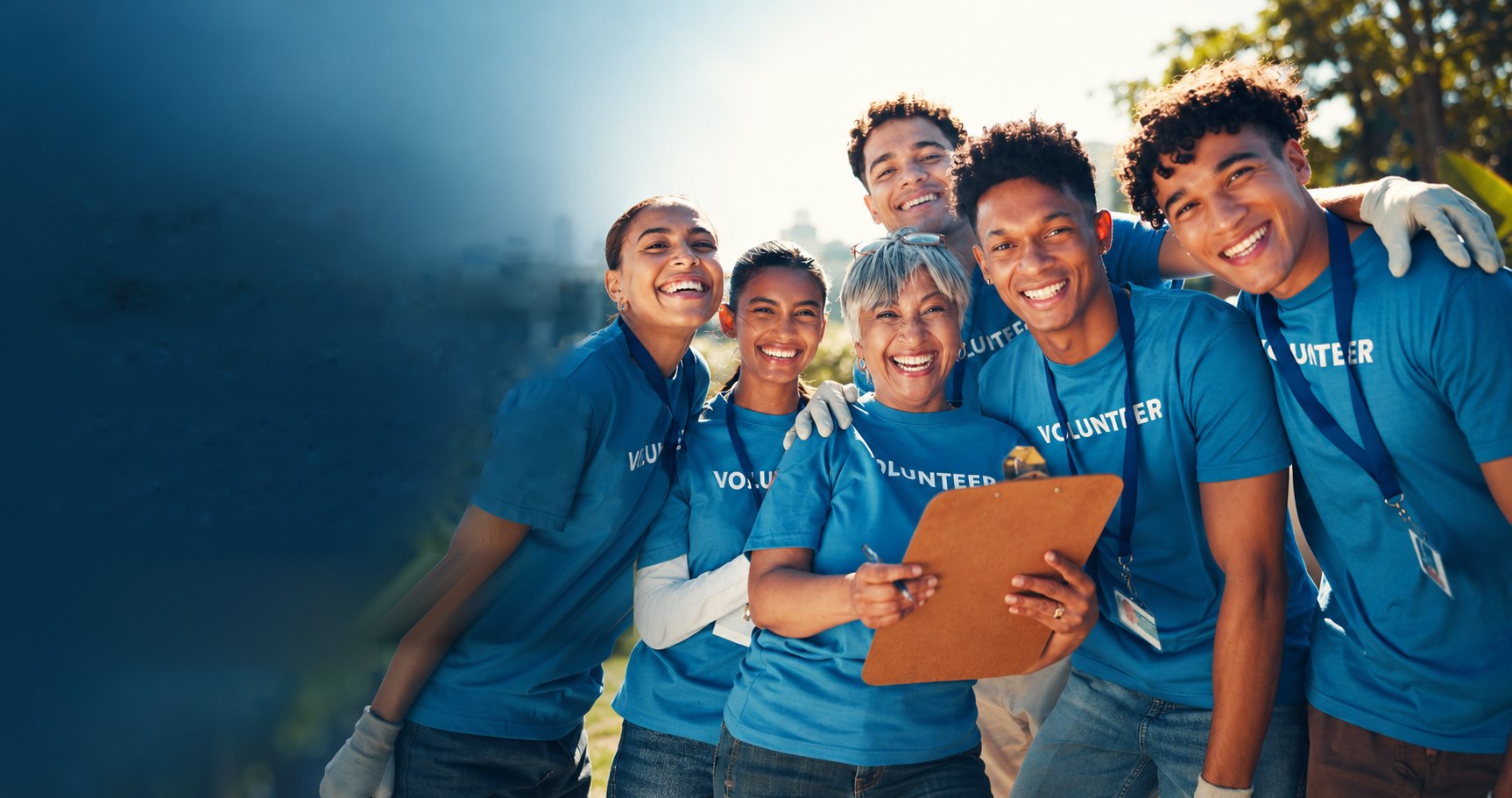Smiling team of volunteers in blue T-shirts gathered together outdoors