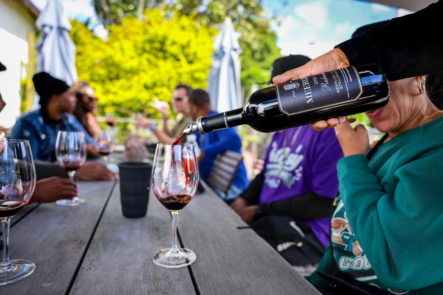Host pouring red wine for a travel group at an outdoor winery tasting table