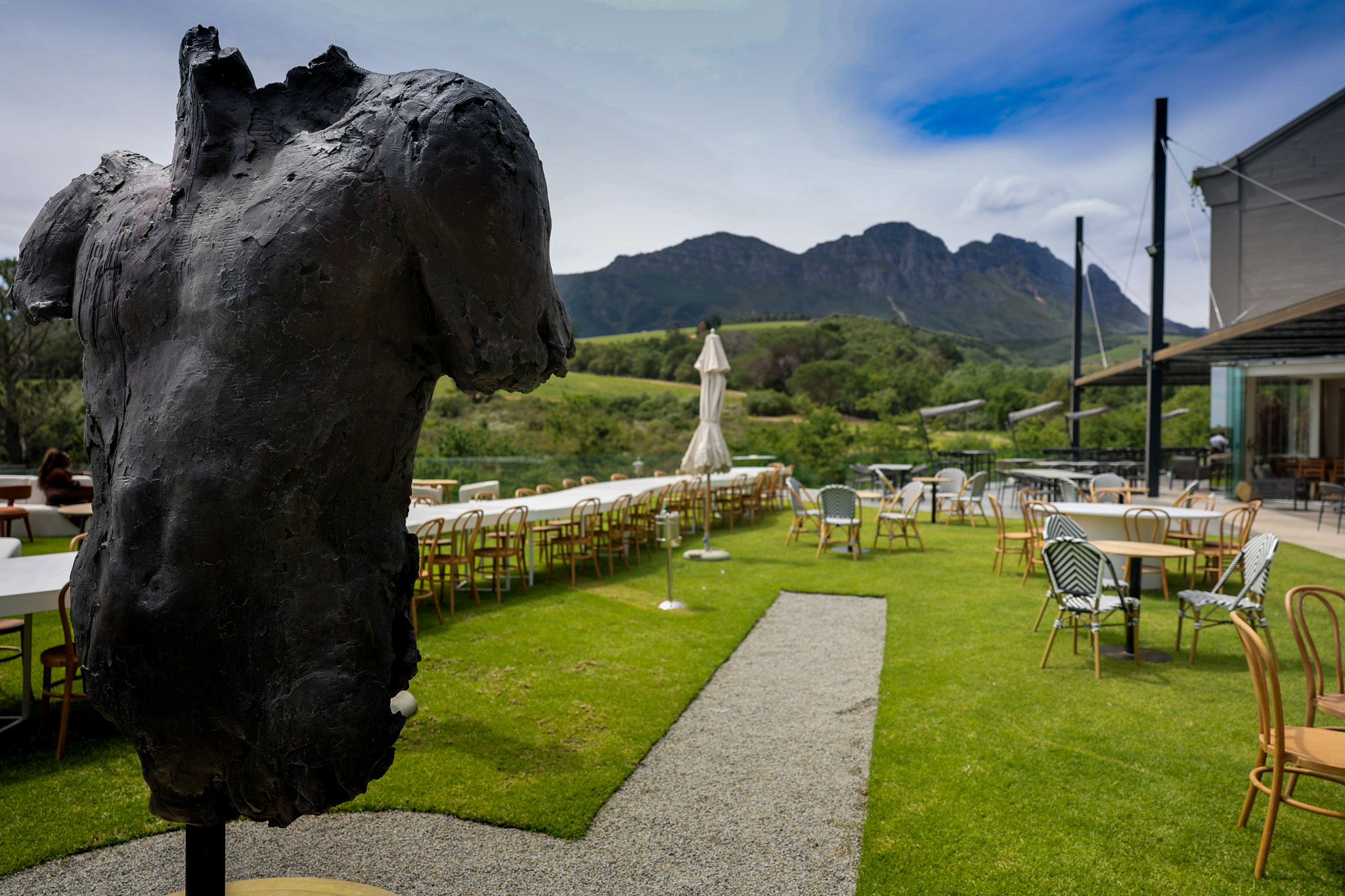 Long banquet tables set on a garden lawn at a mountain view winery, with a bronze sculpture in the foreground